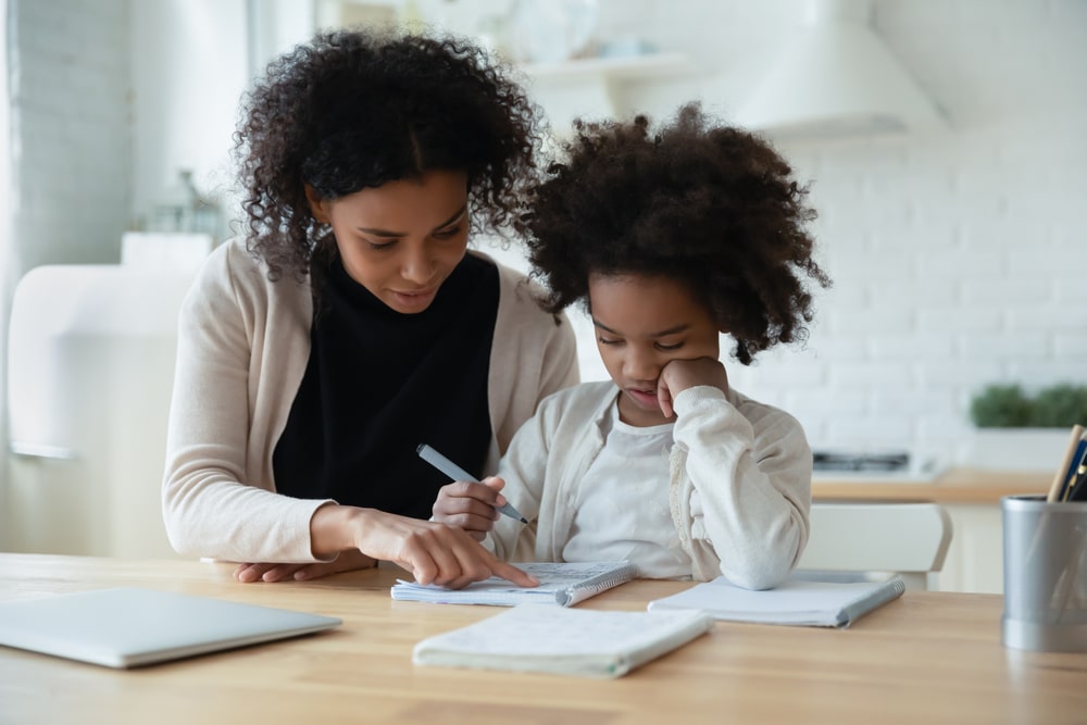 Young girl engaged in a home education lesson with her parent guiding her through a workbook.