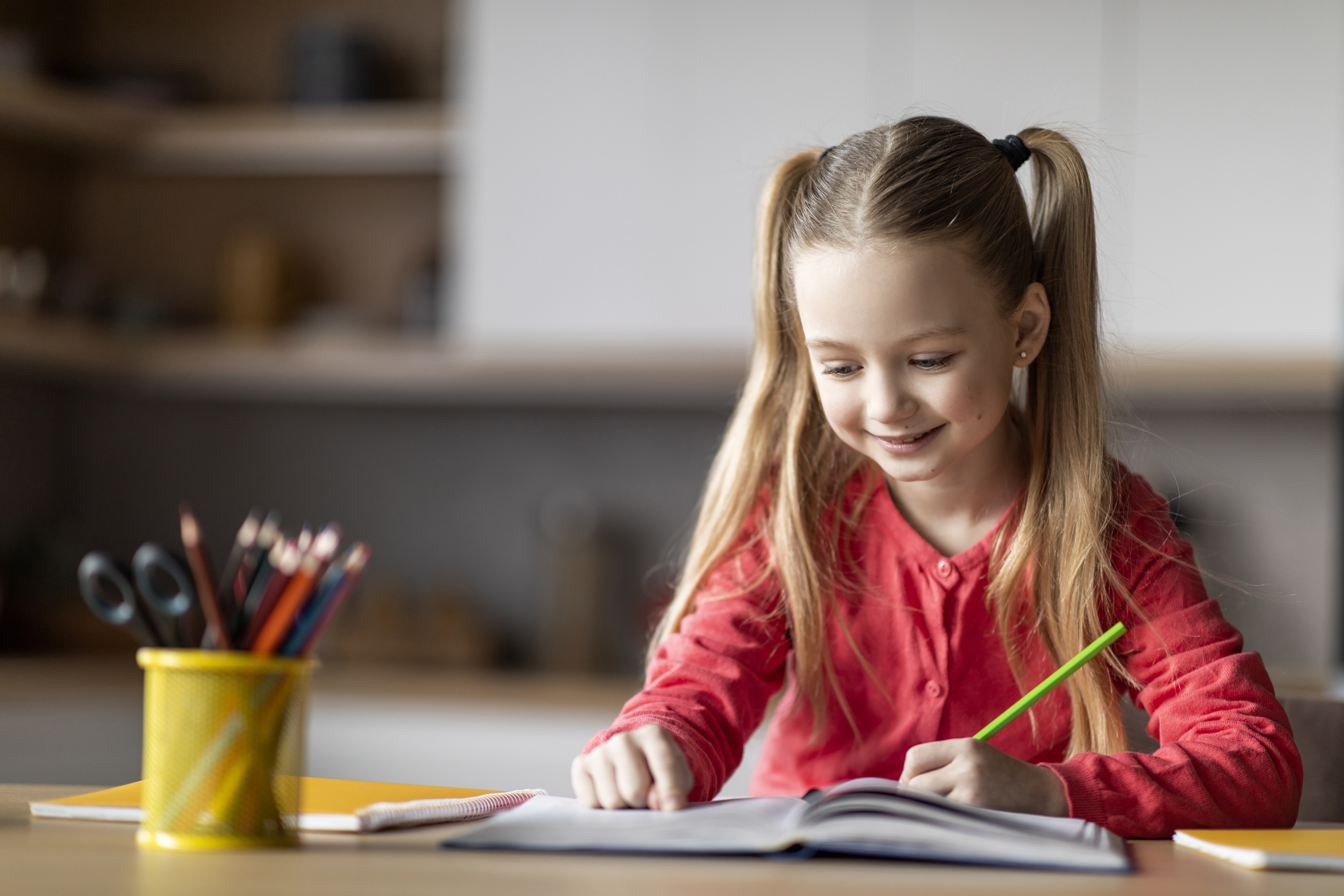 Smiling primary-age girl with pigtails happily writing in a notebook, representing engaging homeschooling for primary children