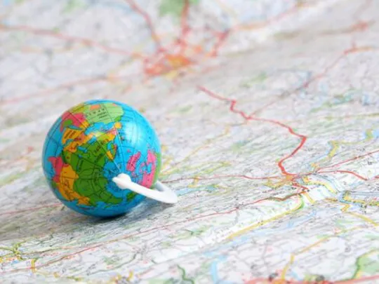 A small sized globe, on top of a large map.