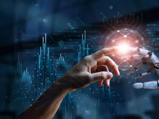 Human hand reaching to touch a robotic hand against a futuristic digital background, symbolising AI and human–machine collaboration