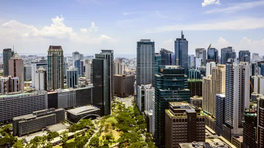 Manila skyline with high-rise buildings and tree-lined roads under a bright blue sky