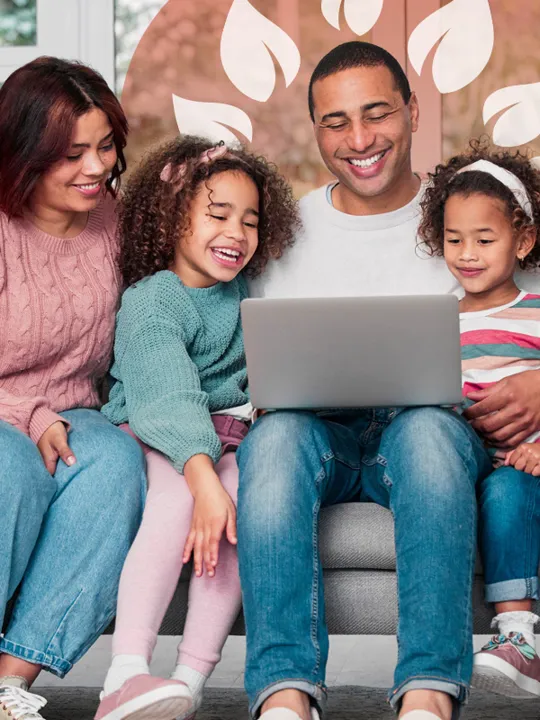 Parents and two young daughters gathered on the sofa enjoying screen time together.