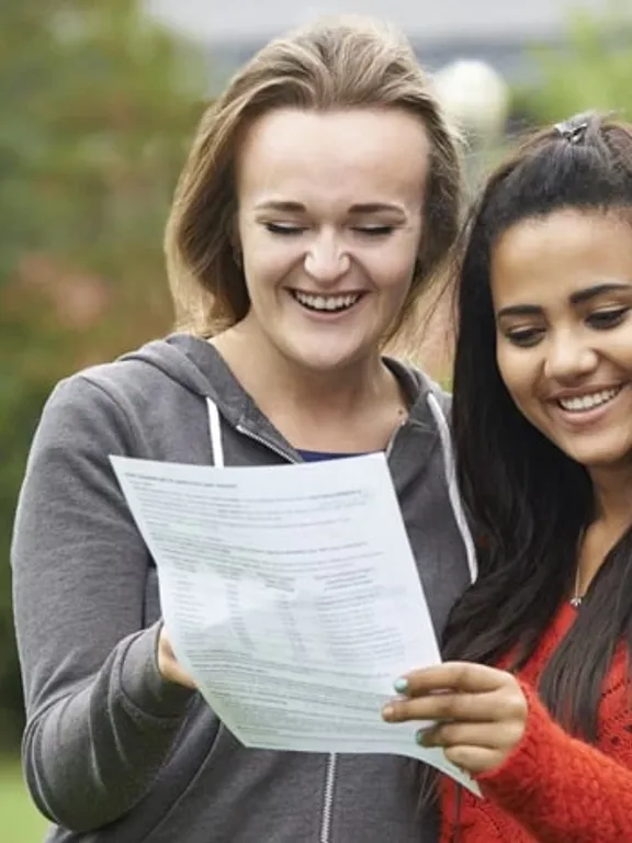 Two homeschooling female students are holding an exam results certificate and smiling.