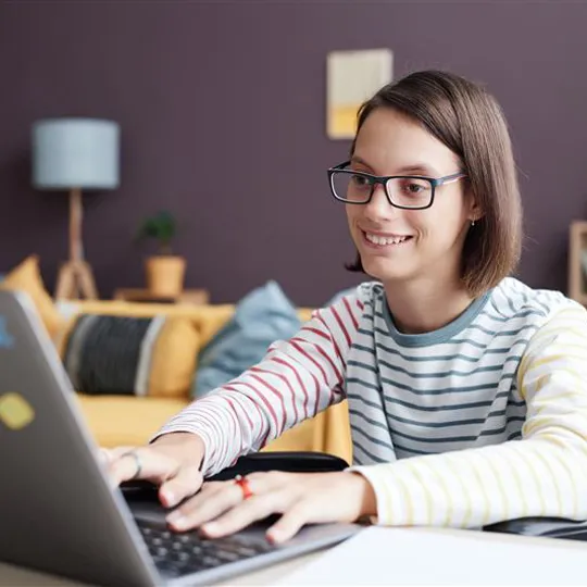 A smiling teenage student in a wheelchair engages happily with her online studies from home.