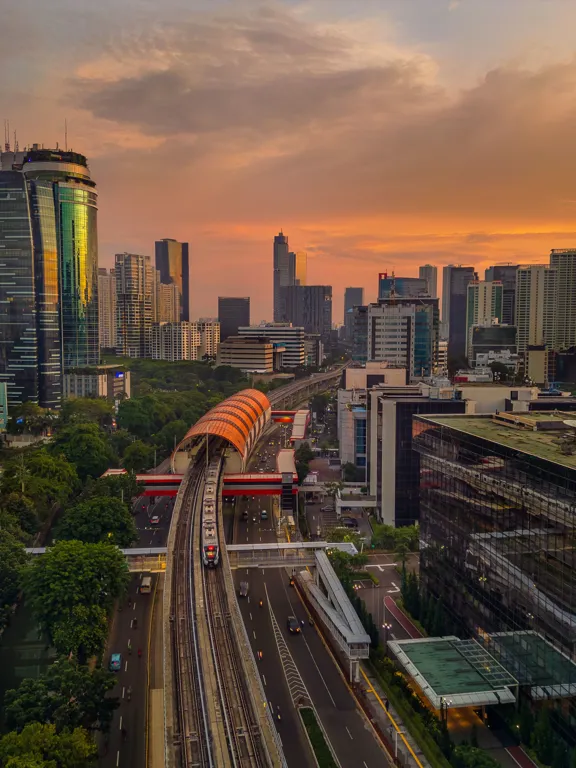 Panoramic sunset view of the Jakarta cityscape with modern skyscrapers and an MRT train, illustrating the vibrant urban setting for families exploring homeschooling options in Jakarta.