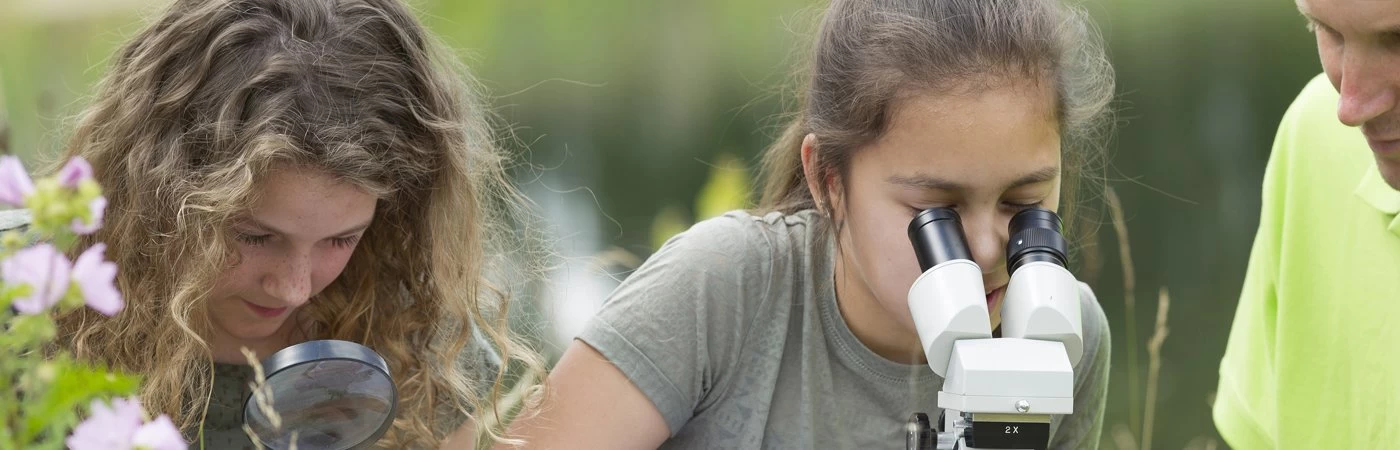 Science students looking through a magnifying glass and microscope. 
