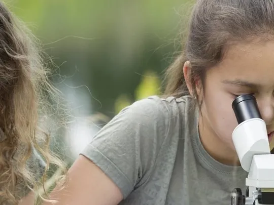 Science students looking through a magnifying glass and microscope.