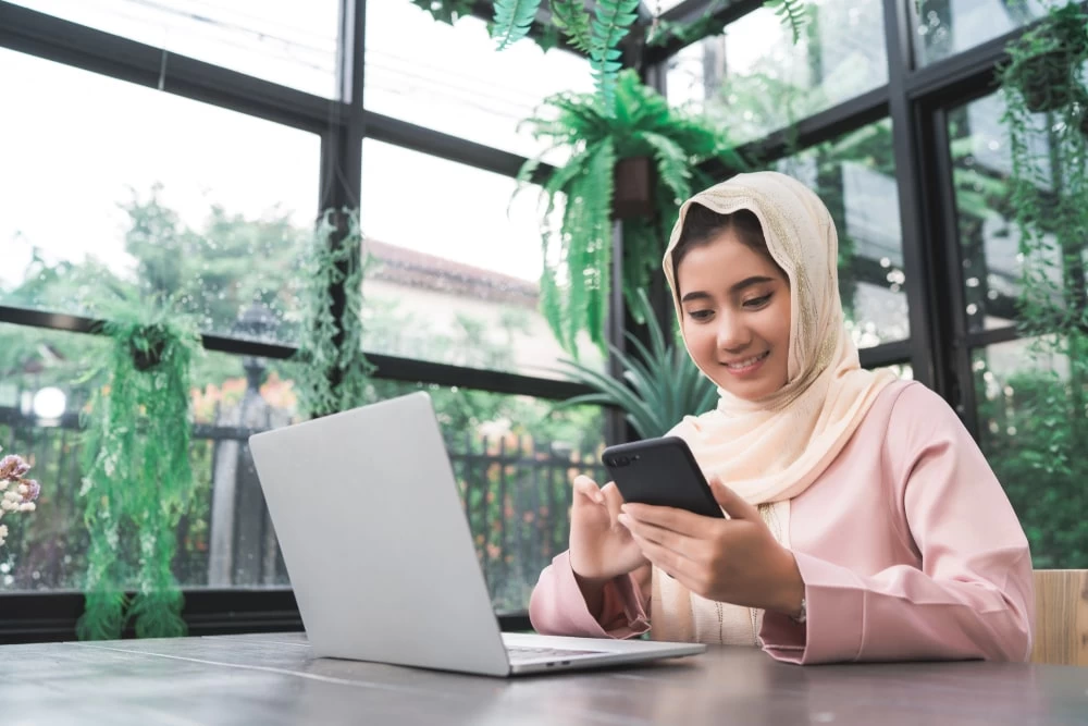 A female student using her laptop and phone for studying. 