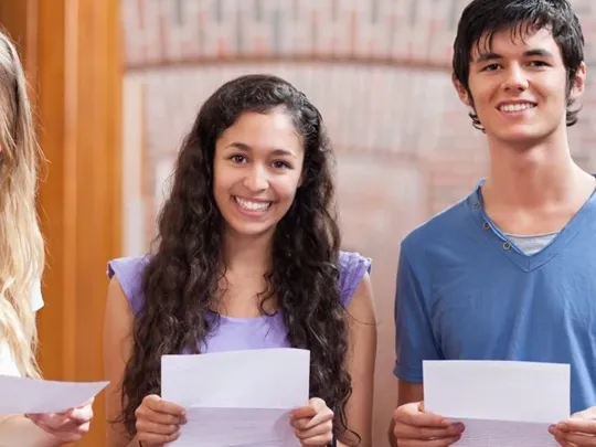 Three teenage students holding their exam results in hand.