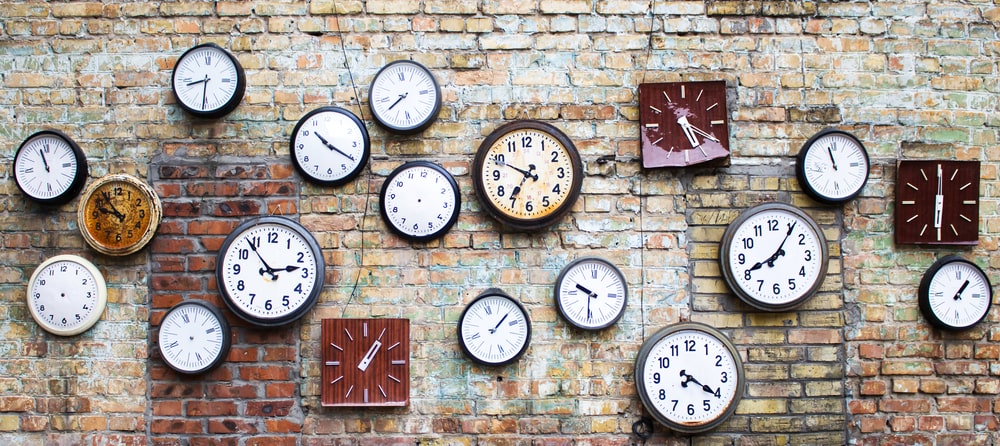 Assorted clocks displaying different times mounted on an exposed brick wall