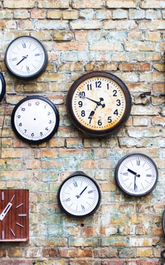 Assorted clocks displaying different times mounted on an exposed brick wall