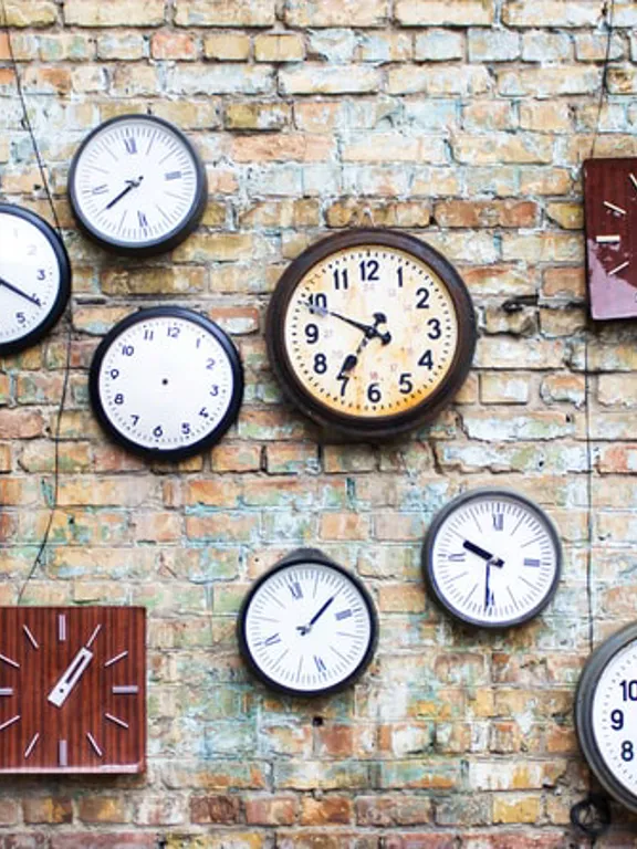 Assorted clocks displaying different times mounted on an exposed brick wall