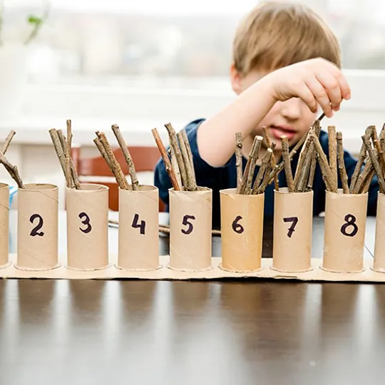 Child placing sticks into cardboard tubes labelled 0 to 10, exploring number recognition and counting