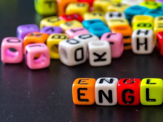 Colourful letter beads scattered on a black surface, with the word “ENGLISH” spelled out in the foreground