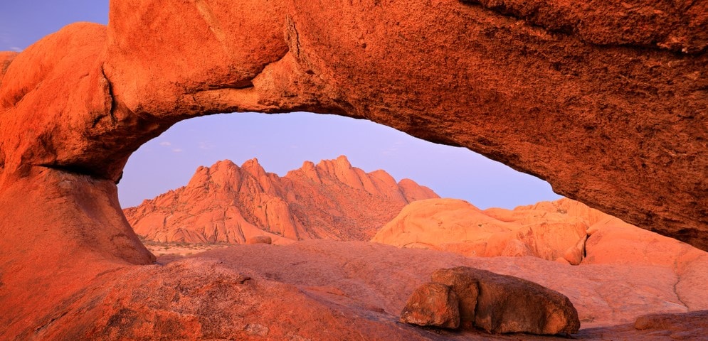 Landscape view of the Namibian desert, with a really bright orange sandy hue and a mountain in the background. 