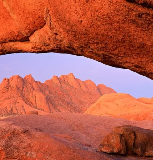 Landscape view of the Namibian desert, with a really bright orange sandy hue and a mountain in the background.