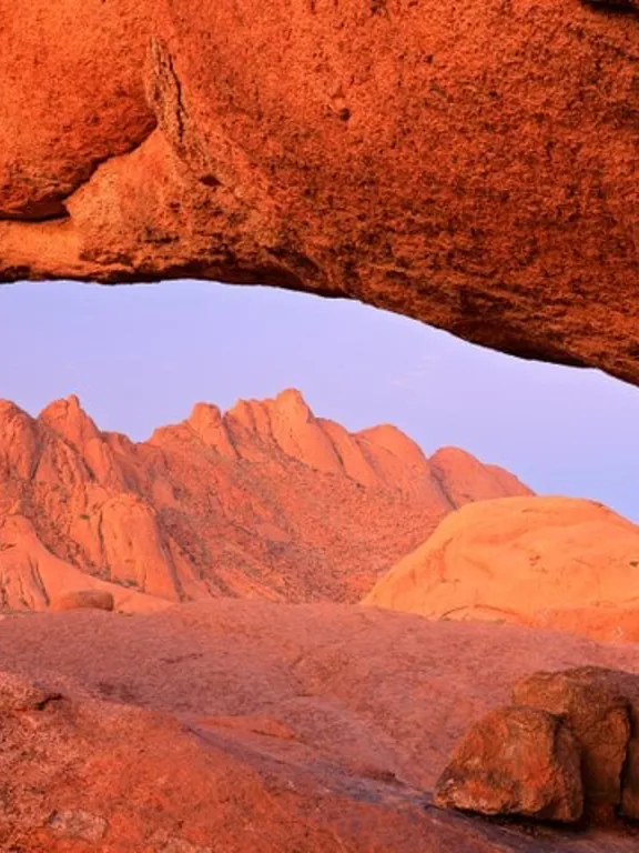 Landscape view of the Namibian desert, with a really bright orange sandy hue and a mountain in the background.