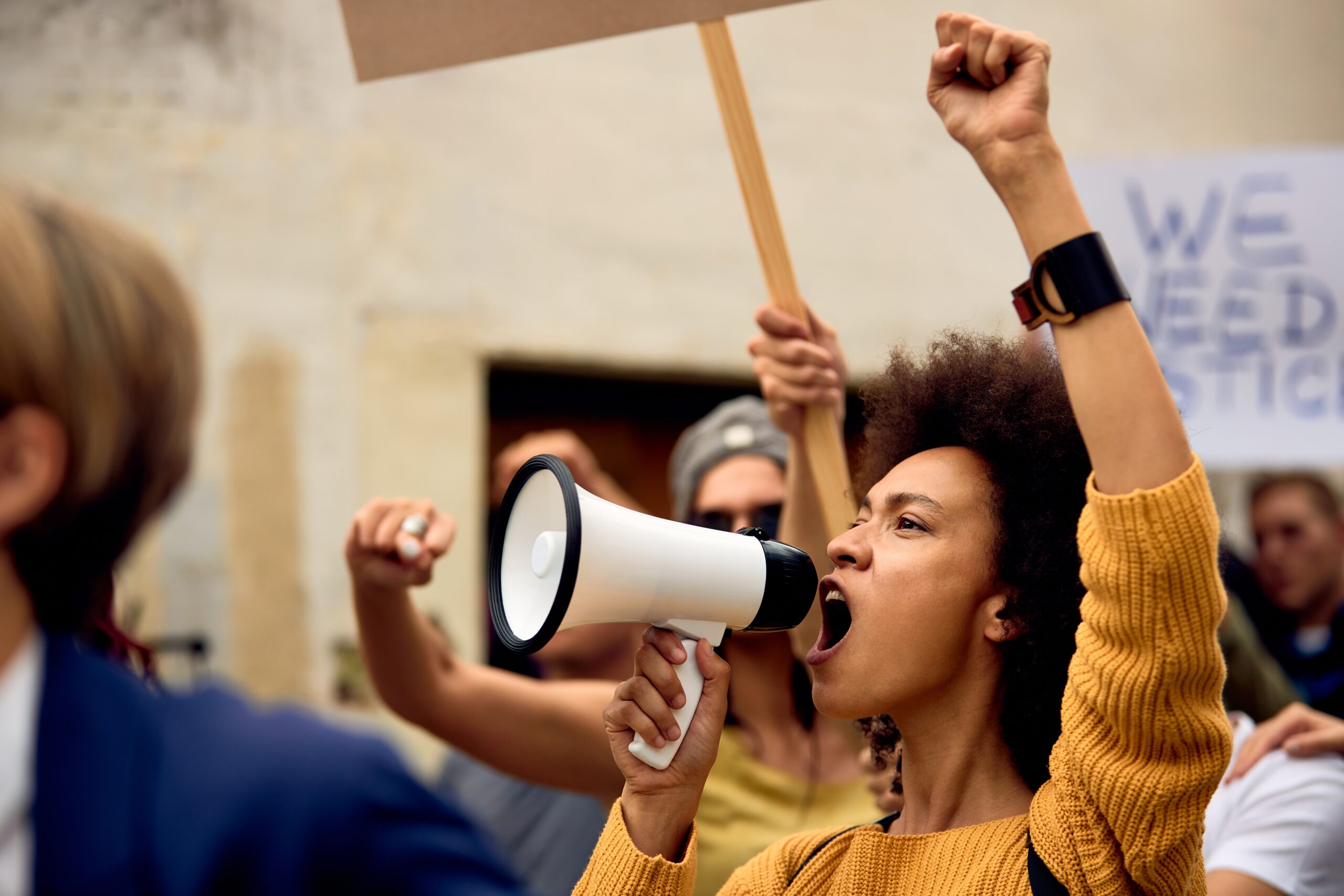Woman raising her fist and speaking into a megaphone during a public protest.