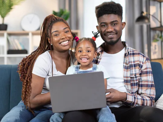 Happy family sitting together on a sofa with their child smiling in front of a laptop