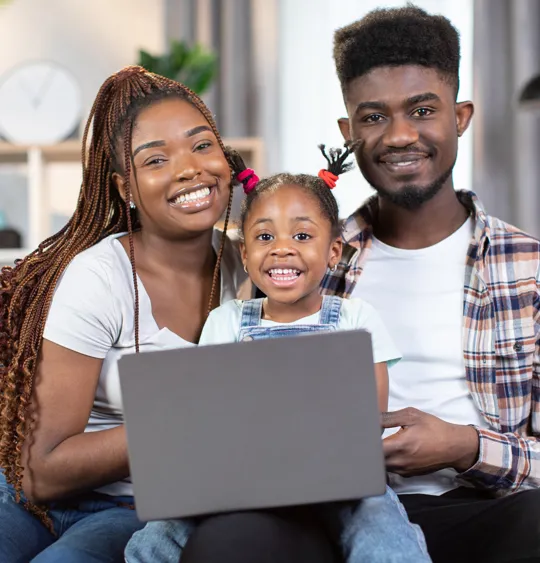 Happy family sitting together on a sofa with their child smiling in front of a laptop