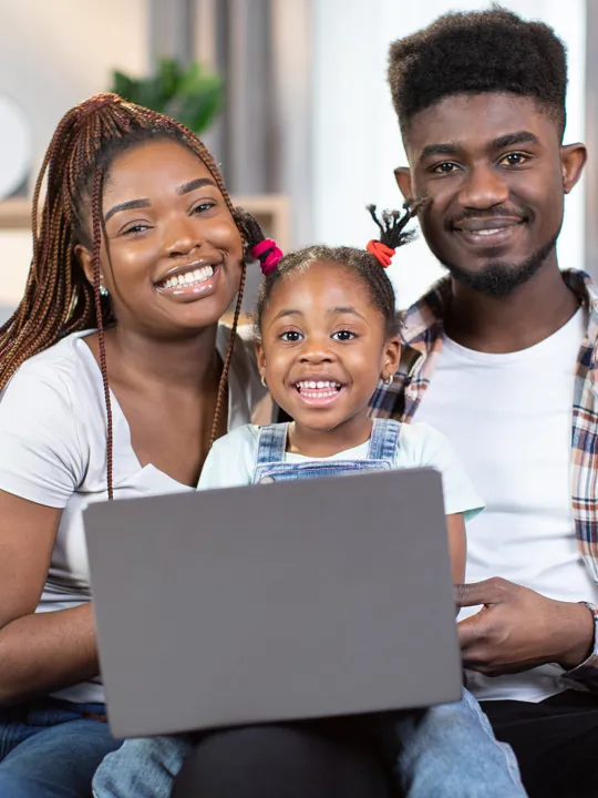 Happy family sitting together on a sofa with their child smiling in front of a laptop