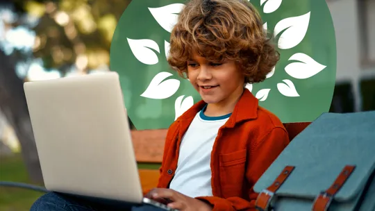 A young student with curly hair, sitting on a bench outdoors and smiling while using a laptop.