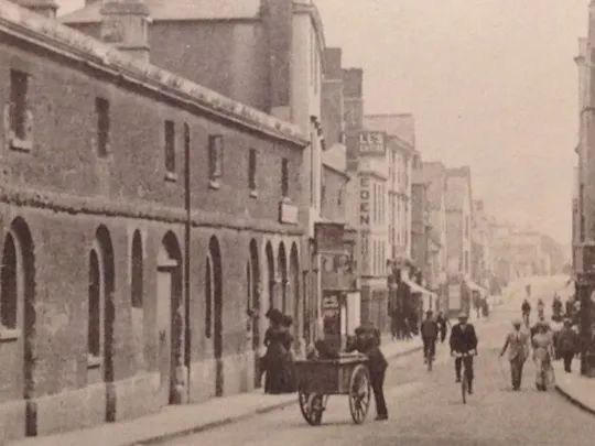 An old sepia landscape photograph of a historic street scene.