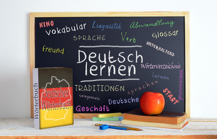 Chalkboard with colourful German vocabulary and the phrase “Deutsch lernen”, next to a dictionary and books.