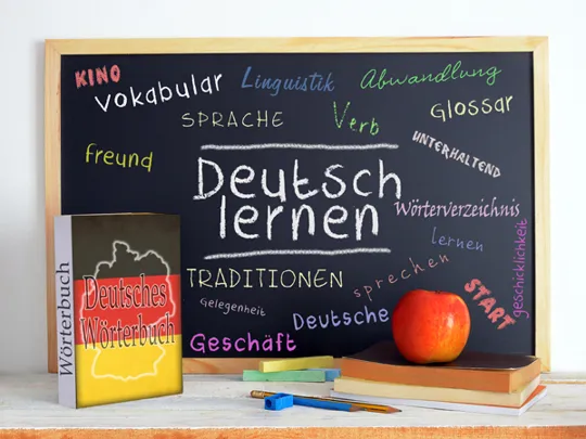Chalkboard with colourful German vocabulary and the phrase “Deutsch lernen”, next to a dictionary and books.