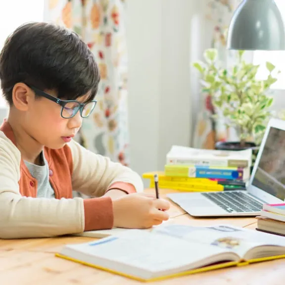 Young male child studying from laptop and making notes.