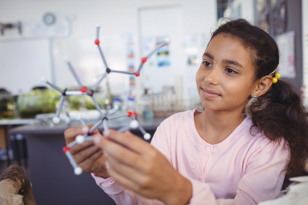 School-aged girl examining a molecular model in a science classroom.