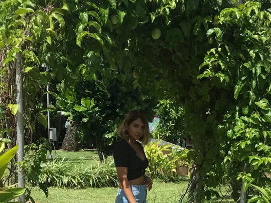 A young woman standing under a green leafy archway with tropical foliage and a glimpse of the ocean in the background in Mauritius.