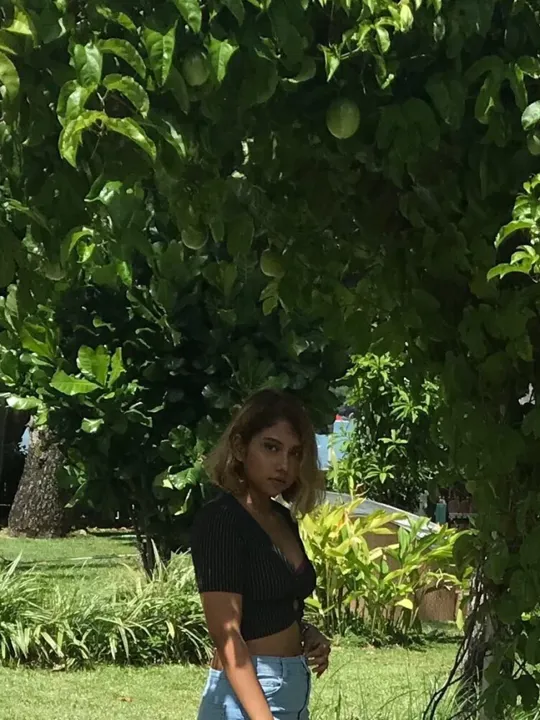 A young woman standing under a green leafy archway with tropical foliage and a glimpse of the ocean in the background in Mauritius.