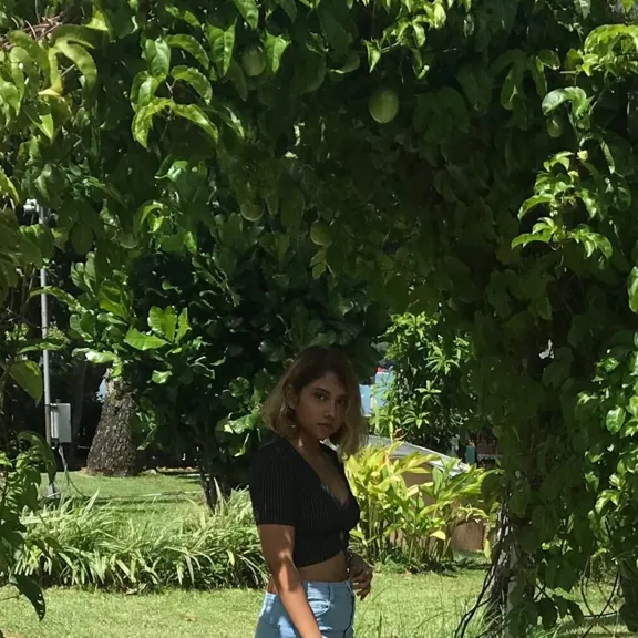 A young woman standing under a green leafy archway with tropical foliage and a glimpse of the ocean in the background in Mauritius.