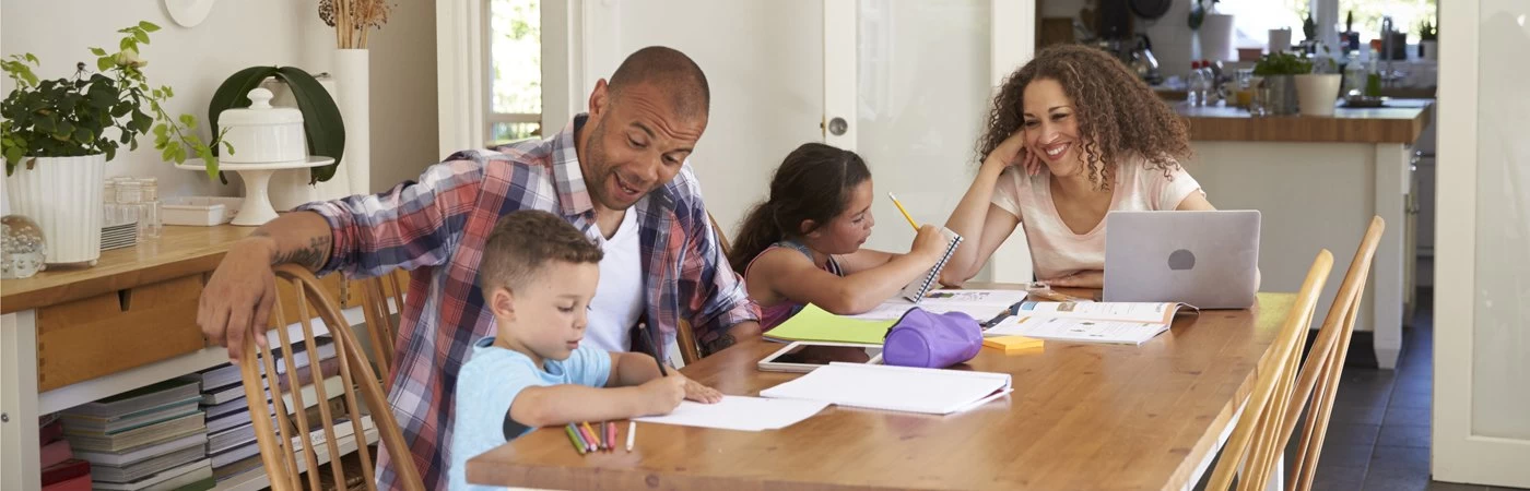 A mum and dad homeschooling their young son and daughter at the kitchen table.