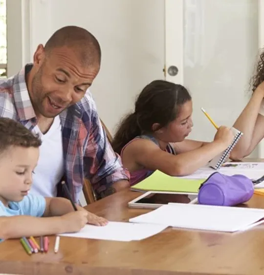 A mum and dad homeschooling their young son and daughter at the kitchen table.