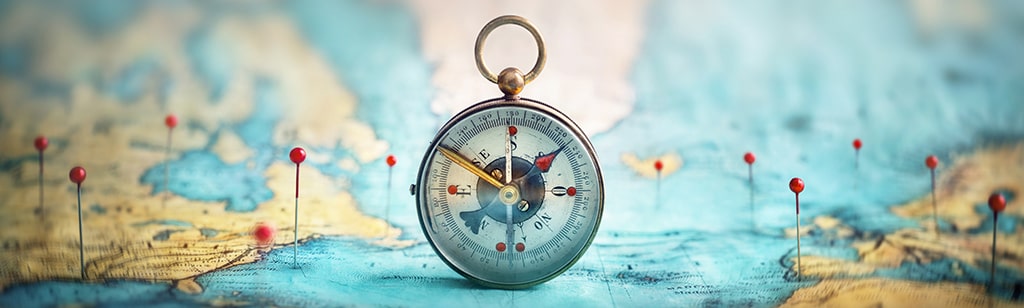 Vintage-style compass placed on a world map, surrounded by red location pins.