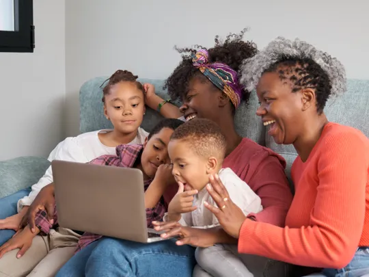 Family of five sharing a moment of learning and laughter together on the sofa with a laptop.