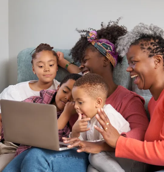 Family of five sharing a moment of learning and laughter together on the sofa with a laptop.