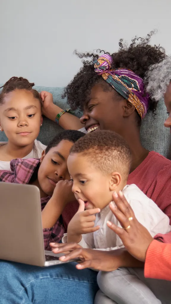 Family of five sharing a moment of learning and laughter together on the sofa with a laptop.