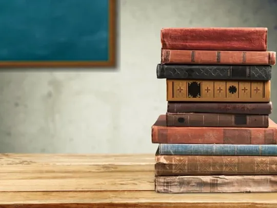 Old English books stacked up on a desk.