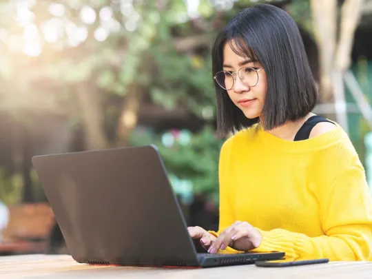 A young person wearing glasses uses a laptop while sitting at a table outdoors, engaged in homeschooling in Penang.