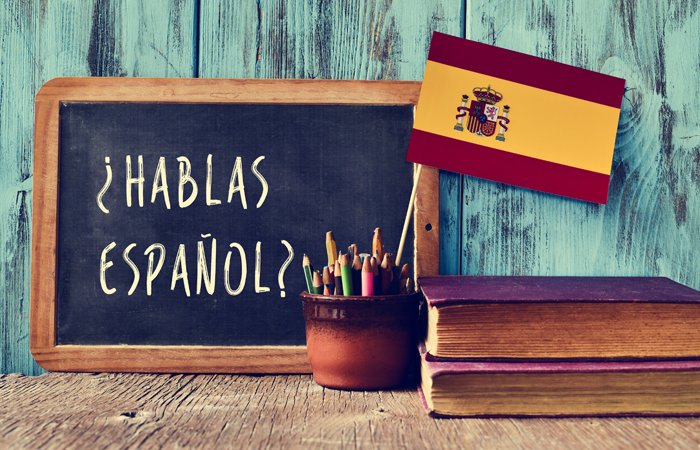 Chalkboard with the phrase “¿Hablas Español?”, next to coloured pencils and a Spanish flag.