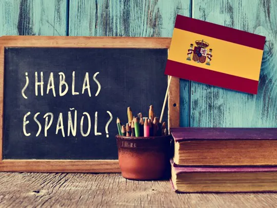 Chalkboard with the phrase “¿Hablas Español?”, next to coloured pencils and a Spanish flag.