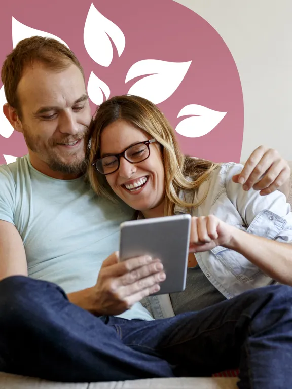 Happy couple sitting on sofa, laughing together while viewing a tablet.