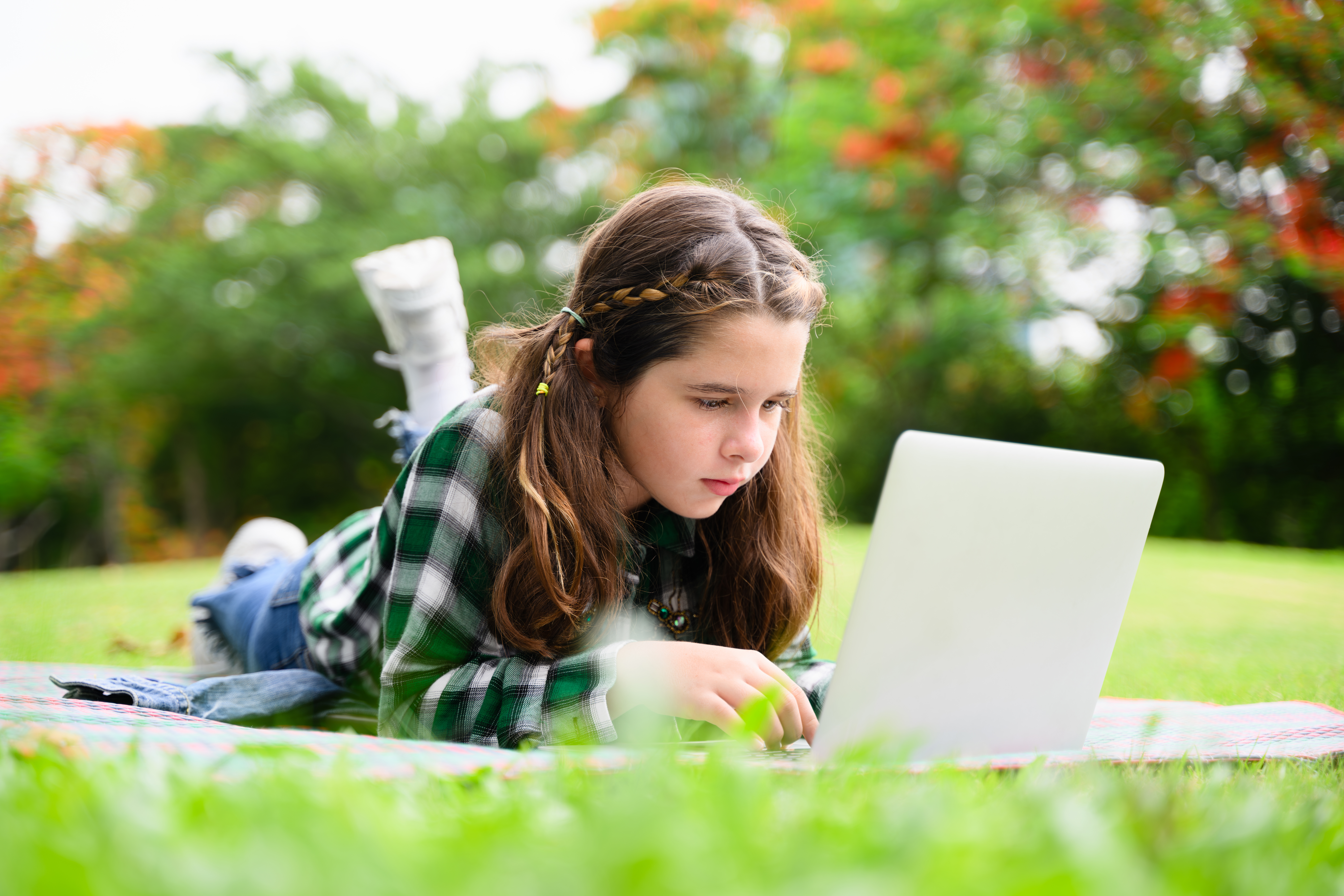 A girl studies comfortably on her laptop in a grassy field, showcasing the flexible learning options available through homeschooling.