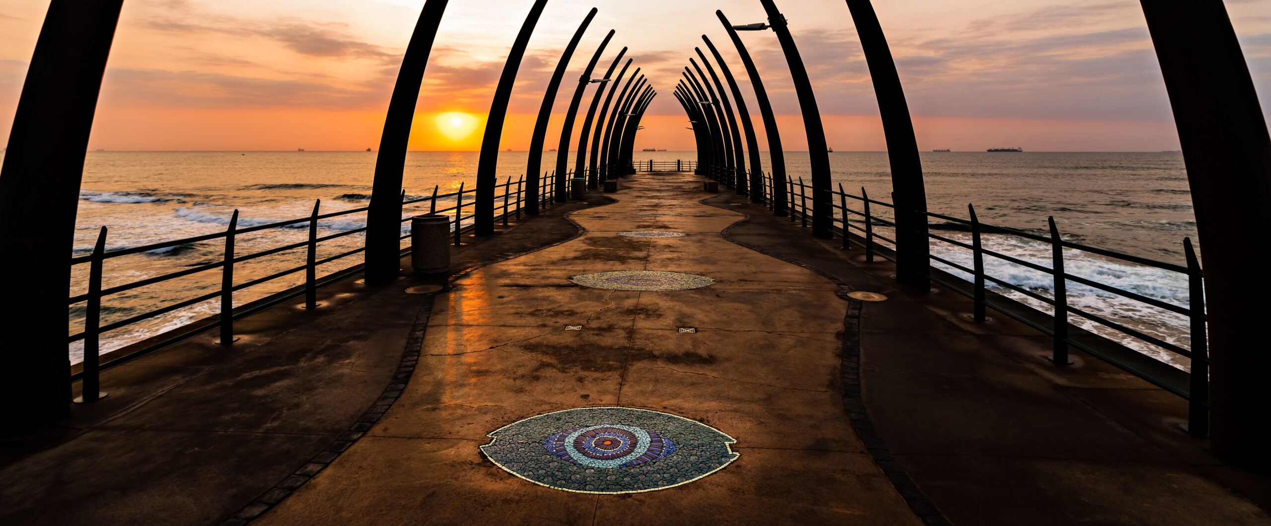 The iconic Whalebone Pier in Umhlanga Rocks, Durban, South Africa, at sunrise or sunset with the sun glowing over the ocean.