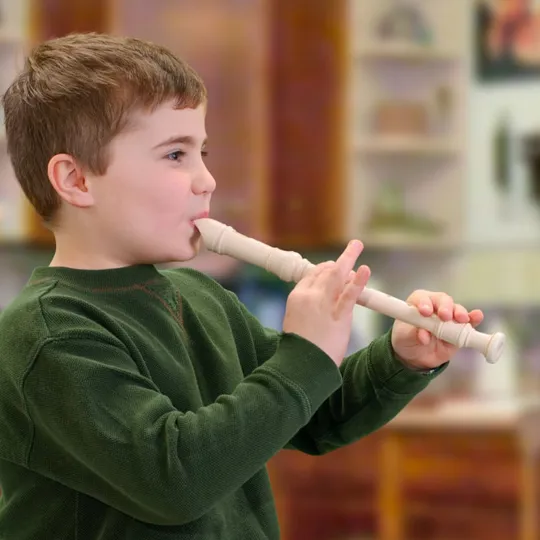 Young boy in a green jumper playing a white recorder in a classroom setting.