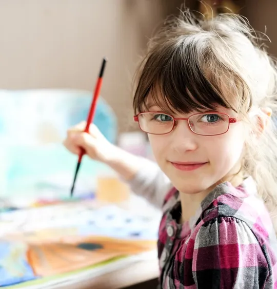 Female child smiling at the camera whilst painting.