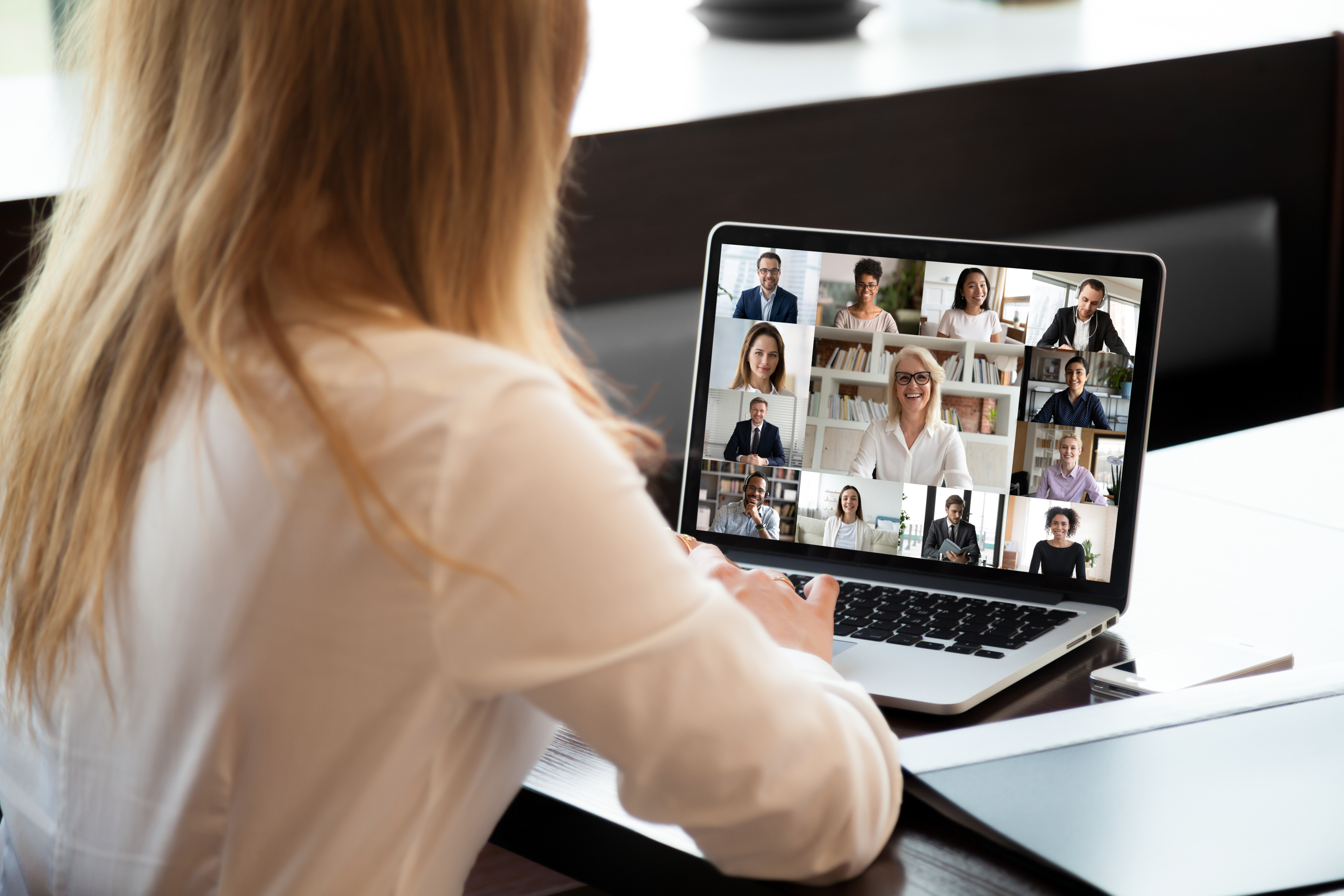 A female employee participates in a virtual team meeting with colleagues on a laptop.